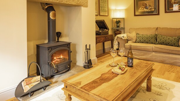 A cozy living room with a wood-burning stove, a wooden coffee table, a sofa, and framed artwork on the wall. - Welcome to The Coach House, a stunning converted coach house and stables in the peaceful village of Staxton, just a short drive from Scarborough and the beautiful Yorkshire Coast. Blending countryside character with contemporary luxury. (Scarborough)