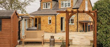 A two-story brick house with a wooden deck, a wooden pergola, and a well-maintained lawn.