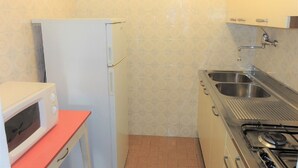 A compact kitchen with a white refrigerator, a microwave, a sink, and a stove.
