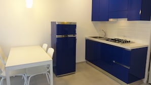 A compact kitchen with a white table and chairs, a blue refrigerator, and a stove. - Modern Flat With sea View (San Michele al Tagliamento)