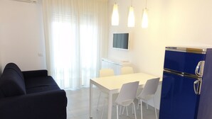 A compact living space with a sofa, dining table, chairs, a TV, and a blue refrigerator. - Modern Flat With sea View (San Michele al Tagliamento)