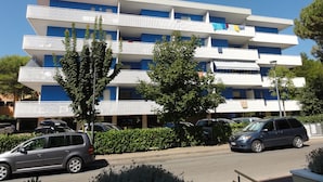 Ein mehrstöckiges Hotel mit Balkonen, parkenden Autos und Grünflächen davor.