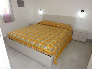 Ein ordentlich bezogenes Bett mit einem gemusterten Überwurf, ein Nachttisch mit Schublade und zwei Wandleuchten.