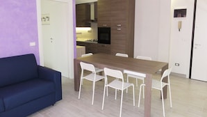 A modern kitchen with a dining area, a sofa, and a door. - Bibione Central Apartment (San Michele al Tagliamento)