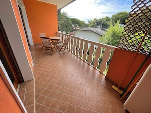 A balcony with tiled flooring, a table with chairs, and a view of greenery and buildings in the background. - Quiet Apartment With Terrace (San Michele al Tagliamento)
