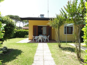 A yellow building with a patio area featuring a table and chairs. - Villa With Fenced Garden in Bibione Pineda (San Michele al Tagliamento)