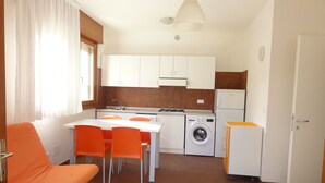 A compact kitchen with a dining area, a washing machine, and a refrigerator. - Villa With Fenced Garden in Bibione Pineda (San Michele al Tagliamento)