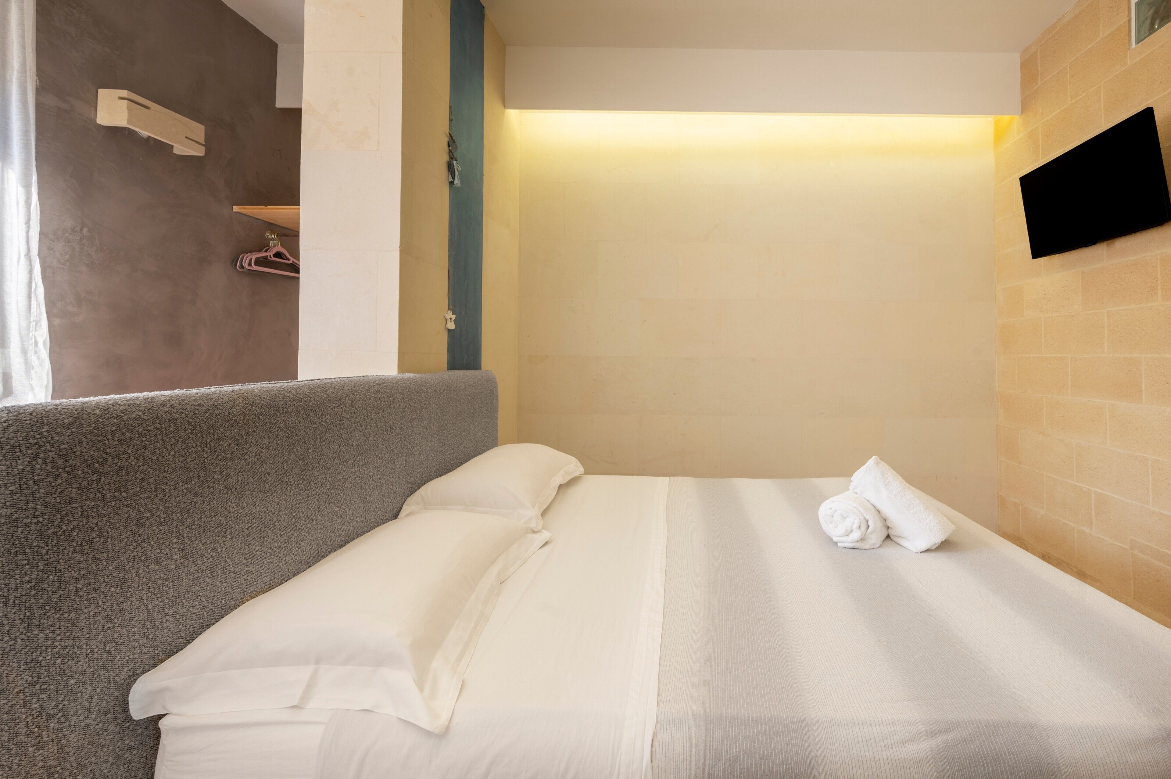 Ein Hotelzimmer mit Bett, Kissen, Handtuch, einem an der Wand befestigten Fernseher und einem Wandregal.