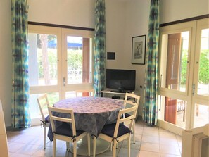 A dining area with a round table, four chairs, a flat-screen TV, and a framed picture on the wall. - Bibione Pineda Villa With Porch and Garden (San Michele al Tagliamento)
