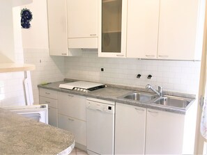 Eine Küche mit weißen Schränken, einem Geschirrspüler von Bosch, einer Arbeitsplatte aus Granit und einer Spüle aus Edelstahl.