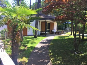 A pathway leading to a covered outdoor seating area with a table and chairs, surrounded by greenery and trees. - Bibione Pineda Villa With Porch and Garden (San Michele al Tagliamento)
