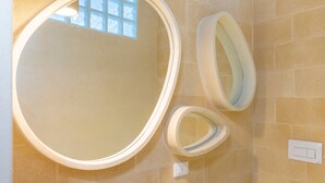 Un baño con un espejo grande, dos espejos más pequeños e interruptor de luz en la pared.