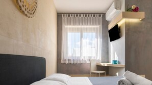 Habitación de hotel con cama, escritorio, silla, televisor y ventana con cortinas.