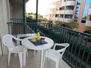 A balcony with a round table and two white chairs, a yellow bottle, and a small container. - Flat in a Modern Coastal Building (San Michele al Tagliamento)