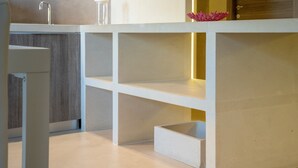 Un baño moderno con un tocador blanco, un espejo y un estante pequeño con un objeto decorativo.