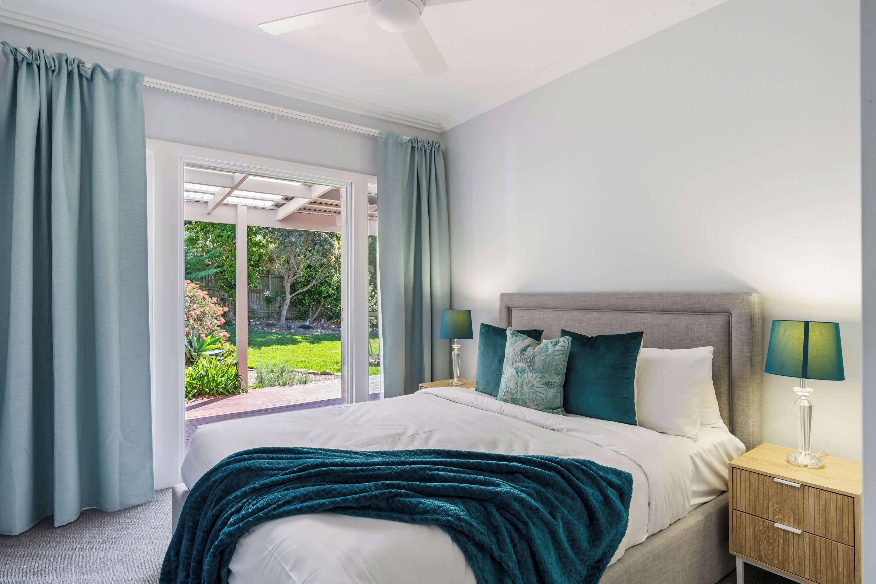 A bedroom with a bed, nightstands, and a view of a garden.