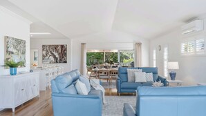 A modern living room with blue sofas, a white cabinet, and a dining area with natural light.