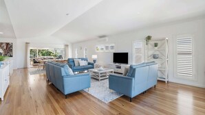 A spacious living room with a blue sofa set, a flat-screen TV, and a dining area in the background.