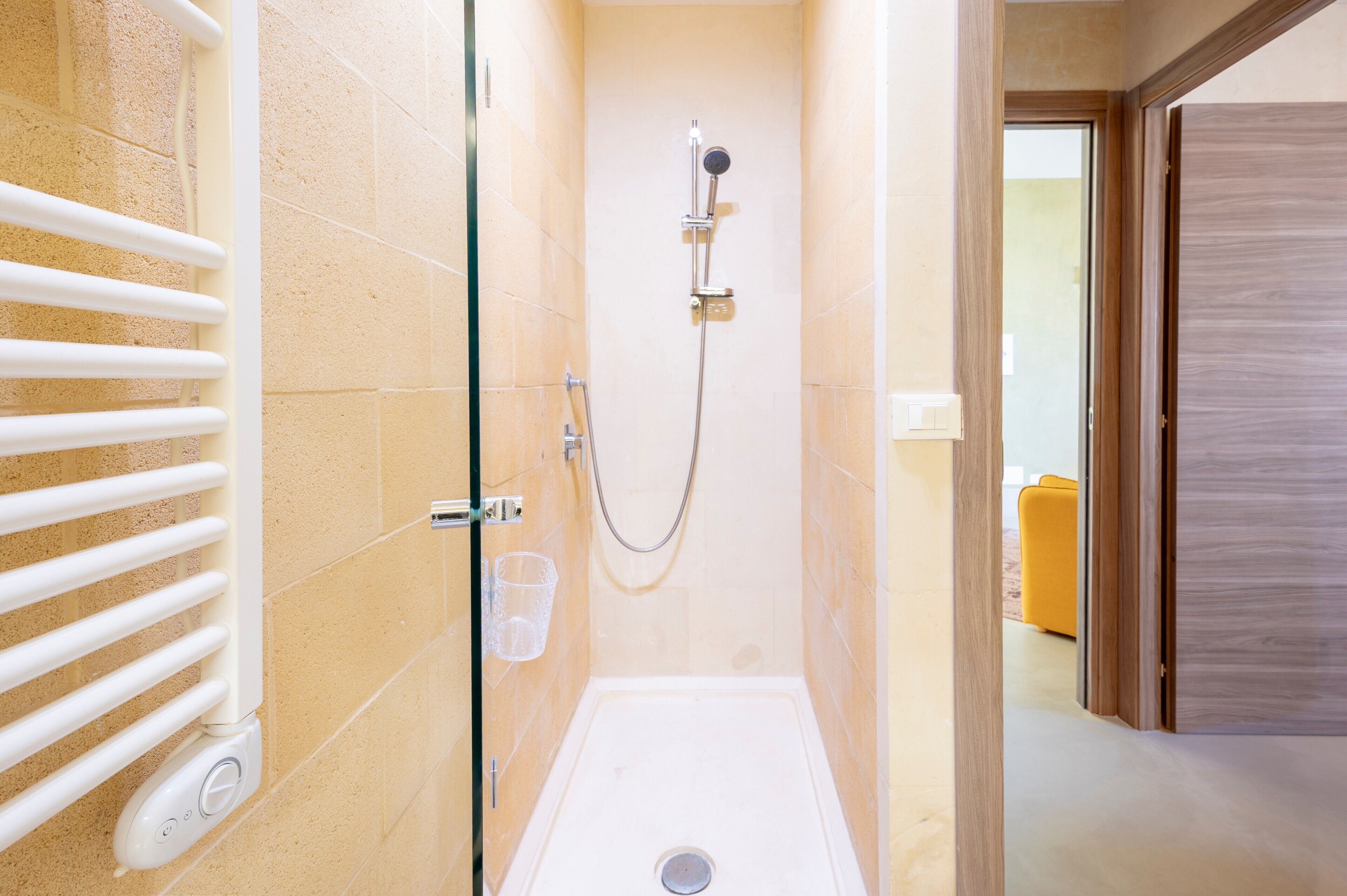 Une douche équipée d’un pommeau de douche à main, d’un récipient en verre et d’un porte-serviettes blanc.