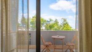A balcony with a table and two chairs, a view of trees and sky through the window, and sheer curtains. - Apartment 'Biancomare Otranto - 5' with Sea View, Wi-Fi and Air Conditioning (otranto)