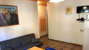 A room with a sofa, a table, and chairs. There is a painting on the wall, a television, and a refrigerator. - Quiet Flat With Garden Access (San Michele al Tagliamento)