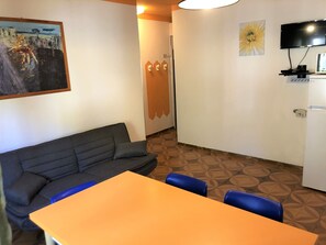 Una habitación con sofá, mesa, sillas, televisión y refrigerador.