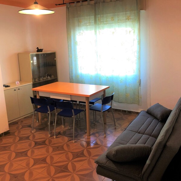 A compact living space with a dining table, blue chairs, a sofa, a cabinet, and a patterned floor.