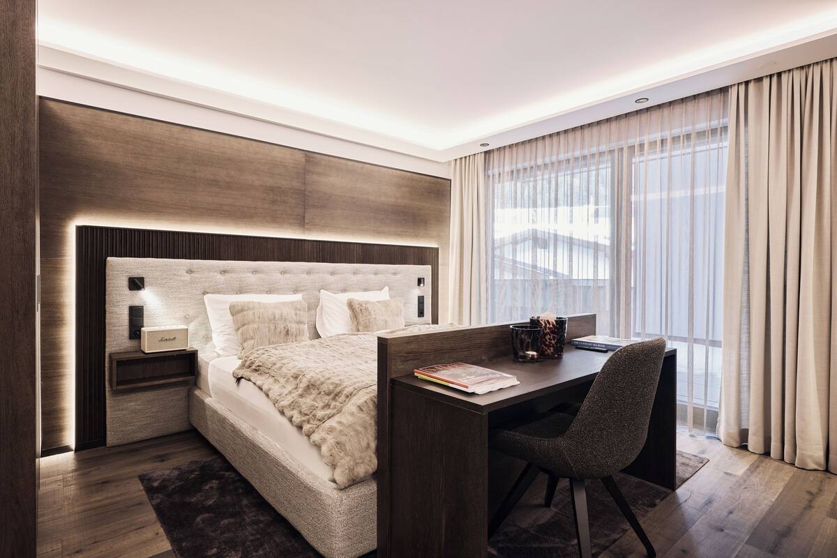 Ein modernes Hotelzimmer mit einem großen Bett, einem Schreibtisch und Blick auf die Stadt durch große Fenster.