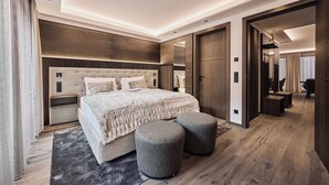 A modern bedroom with a large bed, two ottomans, a wooden headboard, and a mirror. - Chalet Ischgl - Modern Luxury Residences (Ischgl)