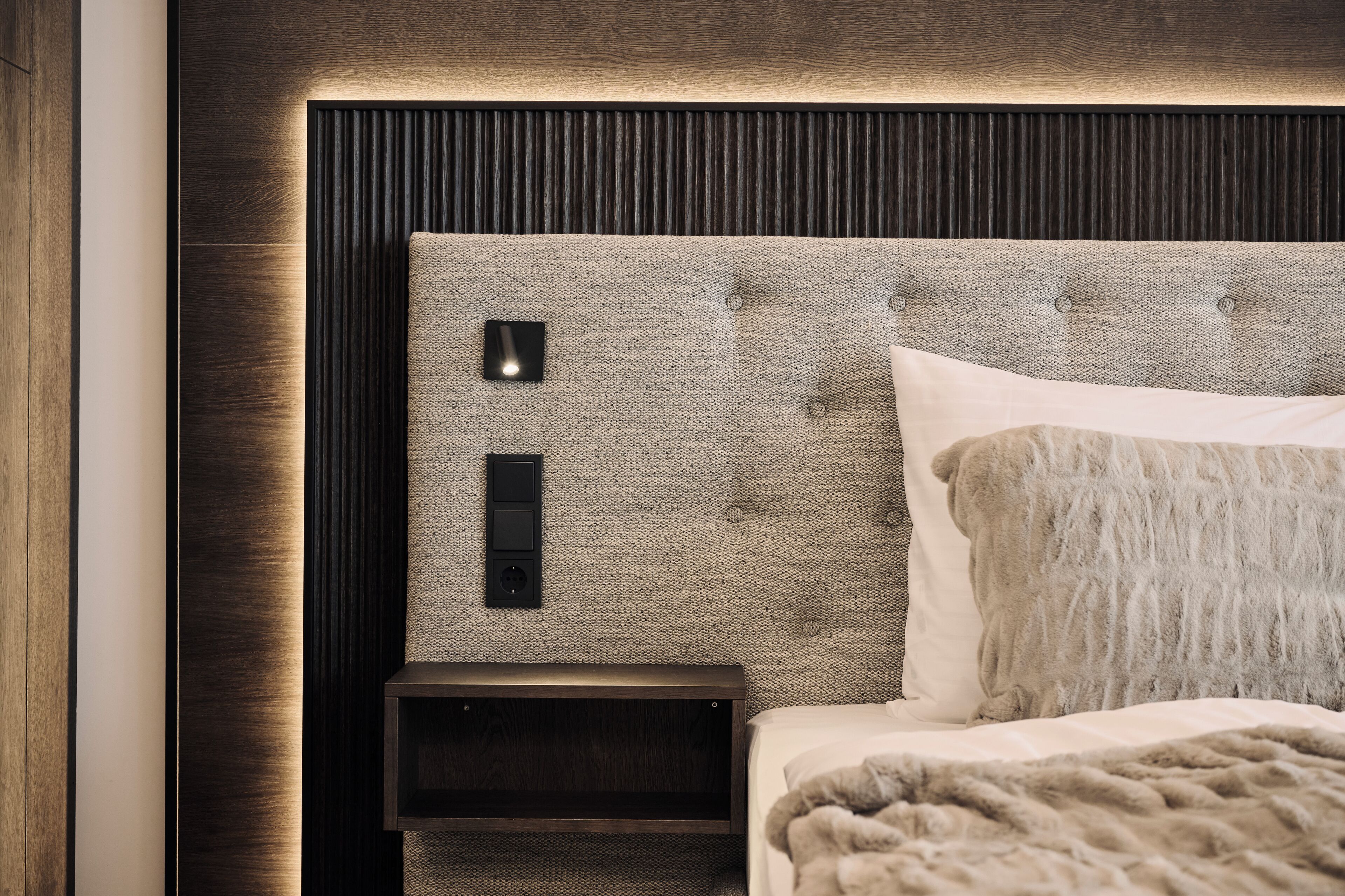 A modern bedroom with a tufted headboard, a bedside table, and a bed with a fluffy blanket.