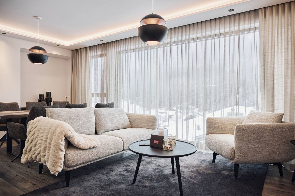 Ein modernes Wohnzimmer mit einer Couch, Sesseln, einem Couchtisch und Pendelleuchten.