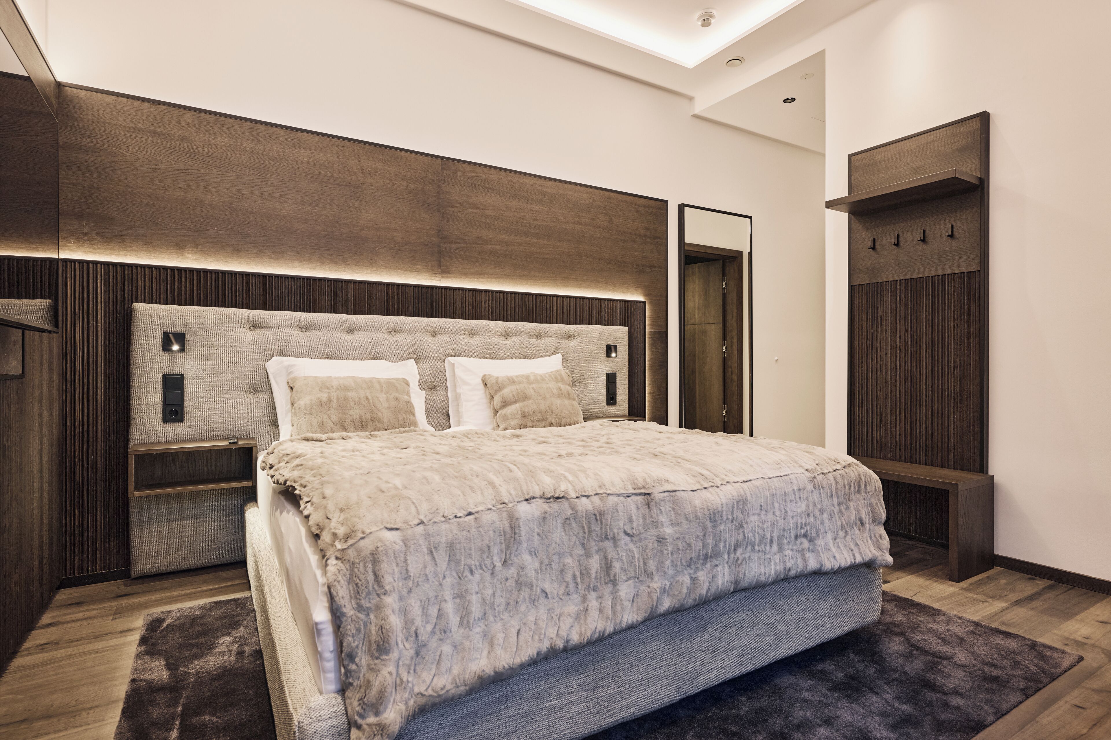 A modern bedroom with a large bed, wooden headboard, bedside tables, and a built-in wardrobe.