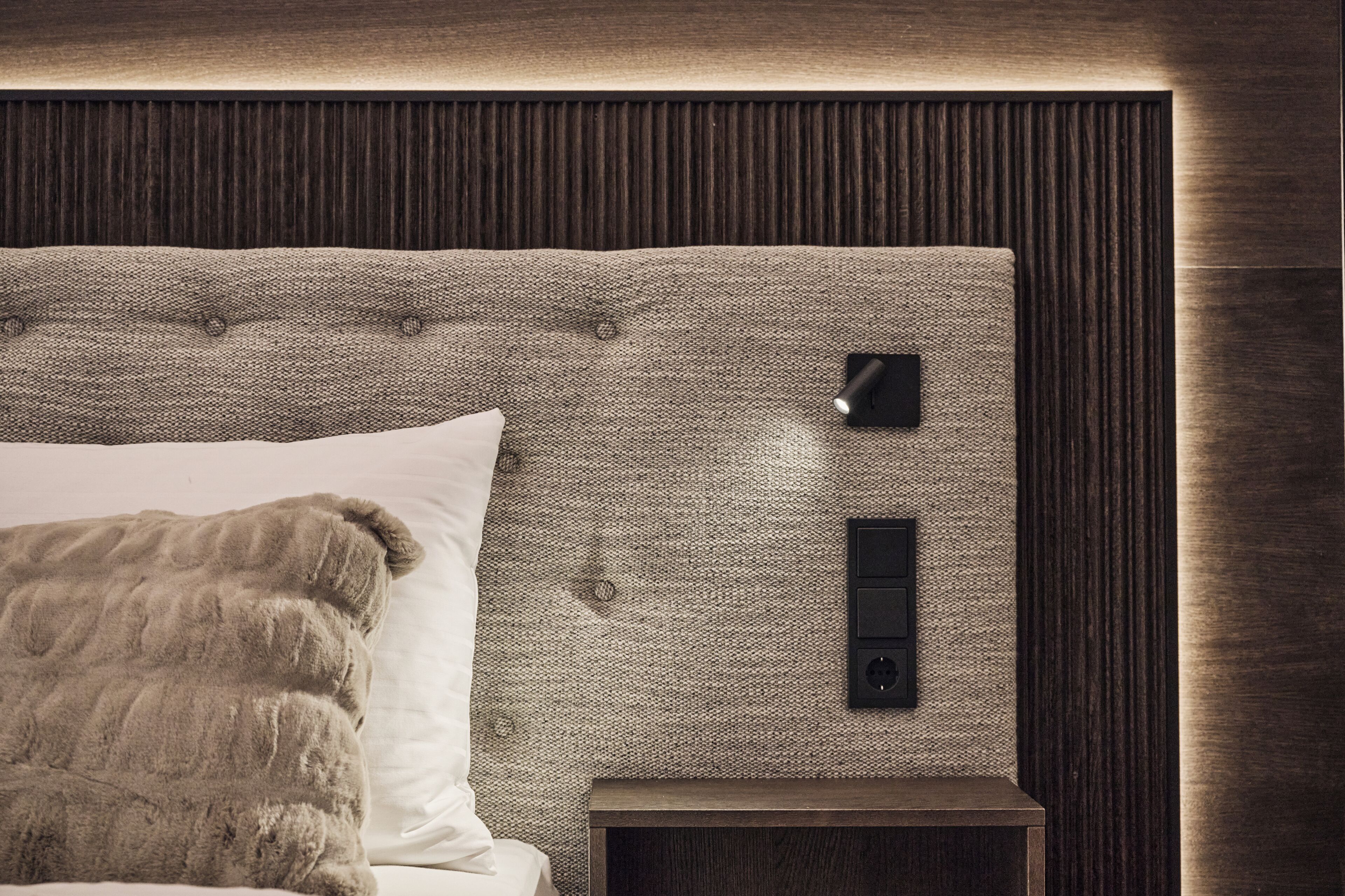 A bedroom with a tufted headboard, a bedside table, and a wall-mounted light fixture.