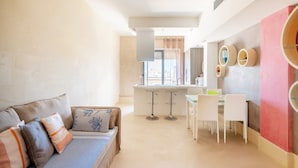 Een moderne woonkamer met een bank, een eethoek met tafel en stoelen, en een keuken met een aanrecht en krukken.