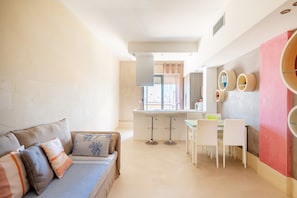 A modern living room with a sofa, a dining area with a table and chairs, and a kitchen area with a counter and stools.