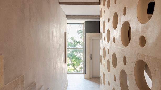 Een hal met een modern ontwerp, met een muur met ronde uitsparingen en een deur naar een andere kamer.