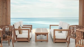 Ein Sitzbereich mit Holzrahmen, weißen gepolsterten Sofas und einem zentralen Tisch, mit Blick auf das ruhige Meer.