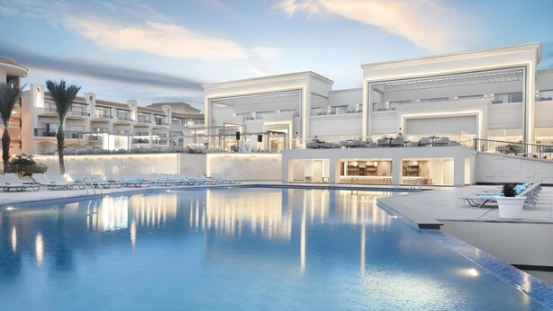 Ein modernes Hotel mit großem Schwimmbad, mehreren Balkonen und einer gut beleuchteten Fassade.