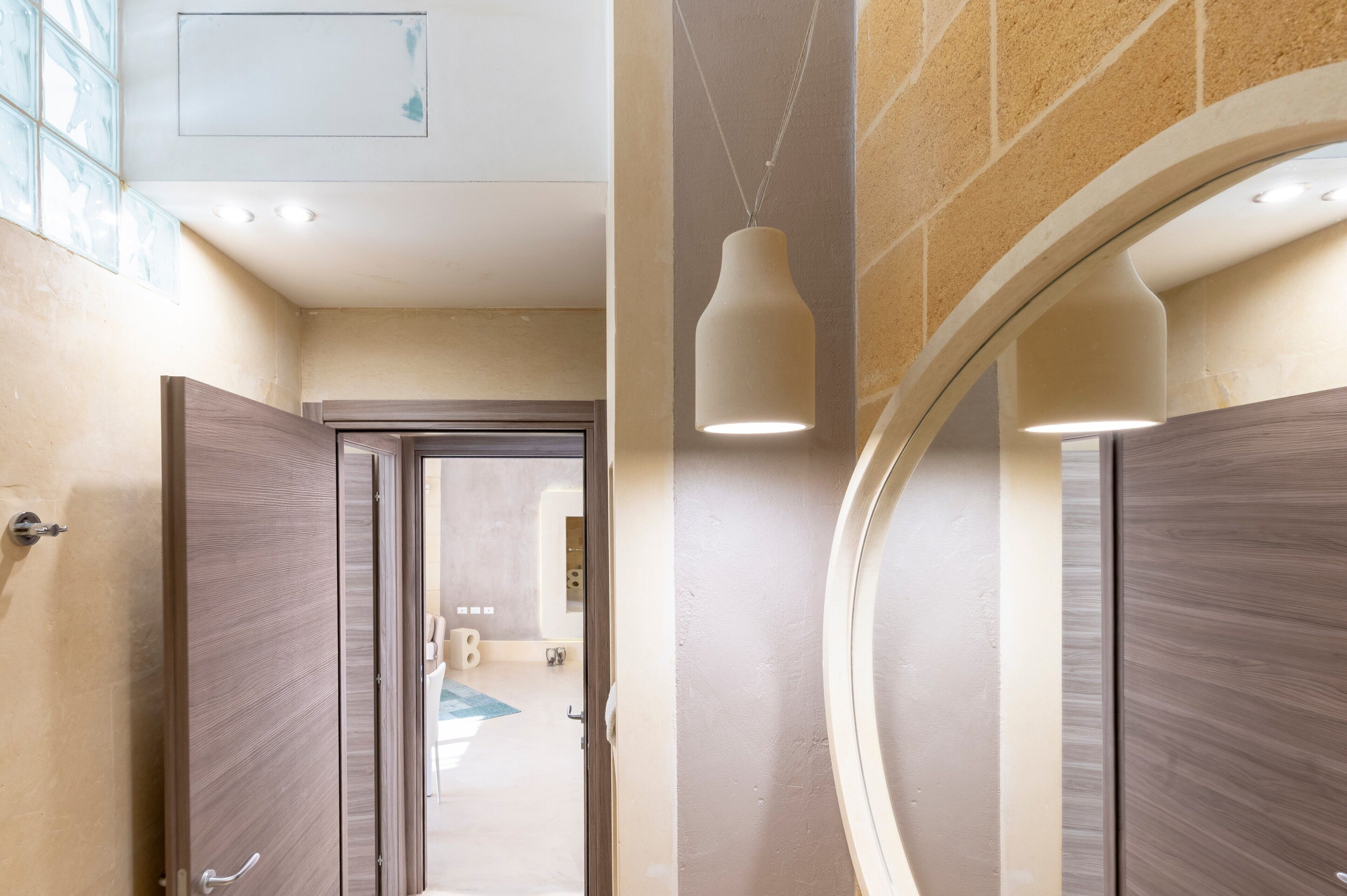 Un couloir d’hôtel avec des portes en bois, un mur en verre et un luminaire suspendu.