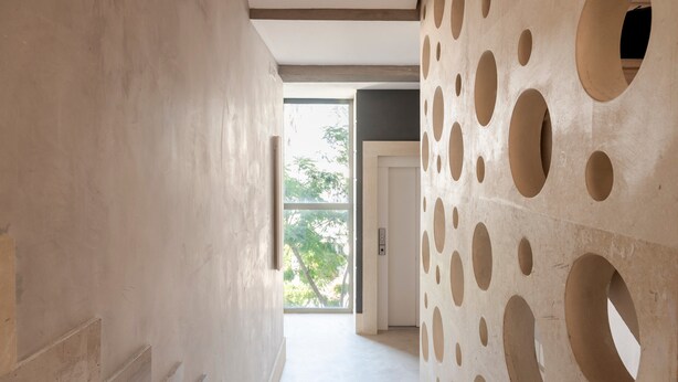 Un pasillo de diseño moderno, con un muro que presenta perforaciones circulares y una puerta que da a otra habitación.