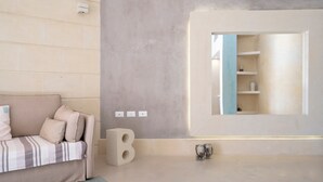 Una habitación moderna con un sofá, una decoración con la letra 'B' de gran tamaño, un estante en la pared y una mesita con un florero.