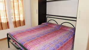 A bedroom with a bed, curtains, a wall-mounted light, and a white wardrobe.