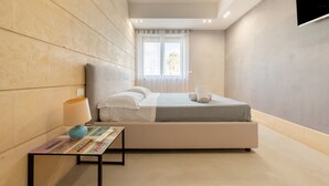 Een moderne slaapkamer met een bed, een nachtkastje met een lamp en een raam met gordijnen.