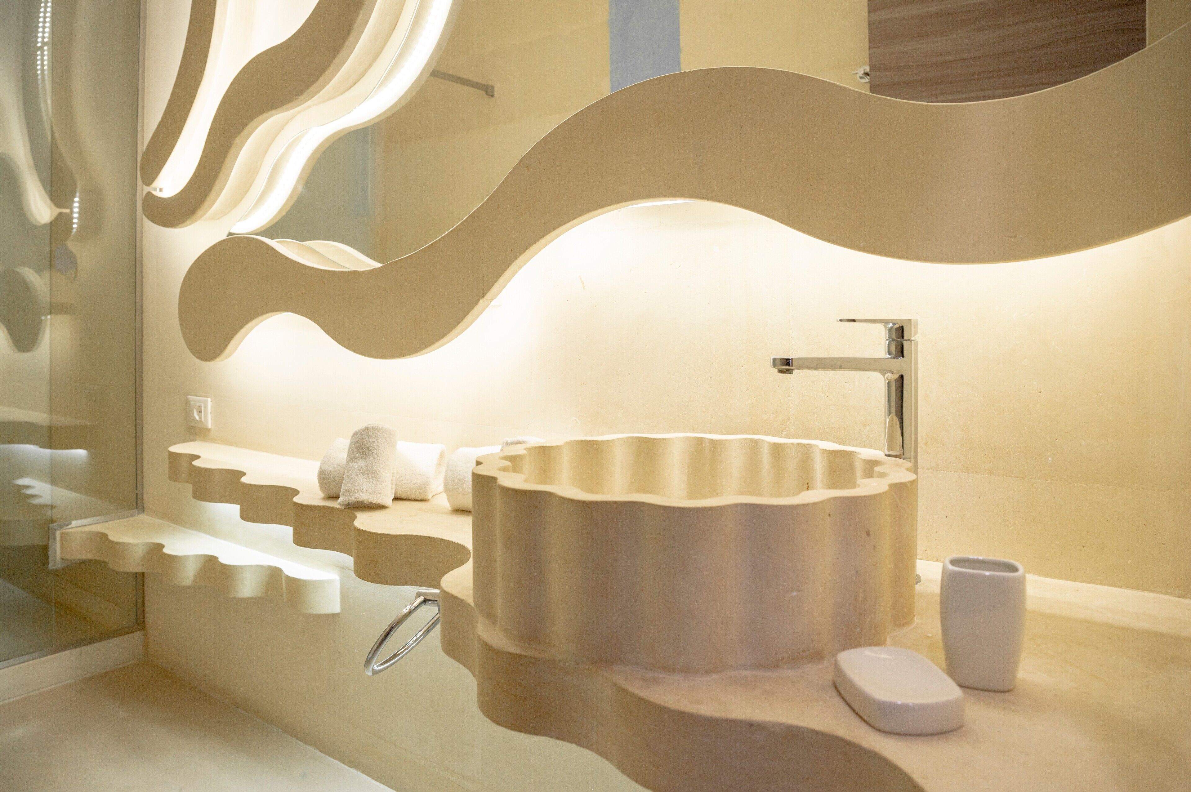 A modern bathroom with a unique wavy mirror design, a round sink, and built-in shelves.