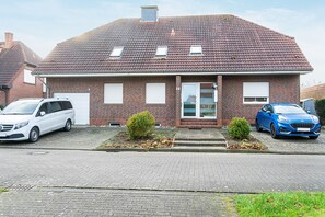 A two-story brick house with a tiled roof, two small bushes, and two parked cars. - Apartment on Two Floors, 60sqm, 2 Bedrooms, Max. 4 Guests (Horumersiel)
