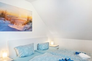 A bedroom with a bed, two bedside tables, a nightstand, and a painting of a beach scene. - Apartment on Two Floors, 60sqm, 2 Bedrooms, Max. 4 Guests (Horumersiel)