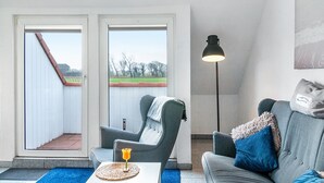 Quarto com sofá cinzento, uma cadeira, abajur e vista através de uma porta.