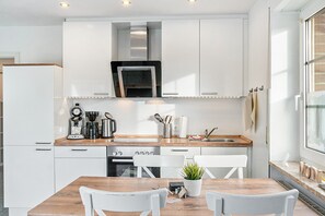 A modern kitchen with white cabinets, stainless steel appliances, and a wooden dining table. - Apartment on Two Floors, 60sqm, 2 Bedrooms, Max. 4 Guests (Horumersiel)