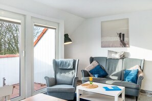 A modern living room with a grey armchair, a grey sofa, and a white coffee table with a blue folder. - Apartment on Two Floors, 60sqm, 2 Bedrooms, Max. 4 Guests (Horumersiel)