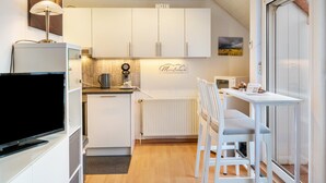 A modern kitchen with white cabinets, a dining area with a table and chairs, a TV, and a radiator. - Meeresfeeling for 2: Cozy North Sea Apartment, 34 sqm, 1 Bedroom, Max 2 Guests (Horumersiel)